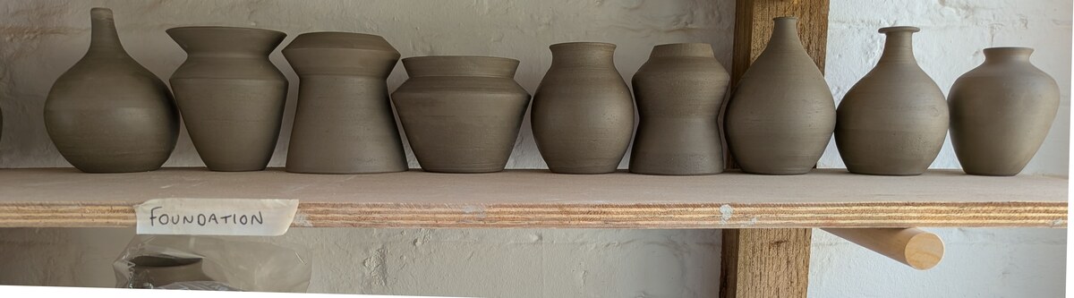 Nine ceramic vases arranged on a studio shelf